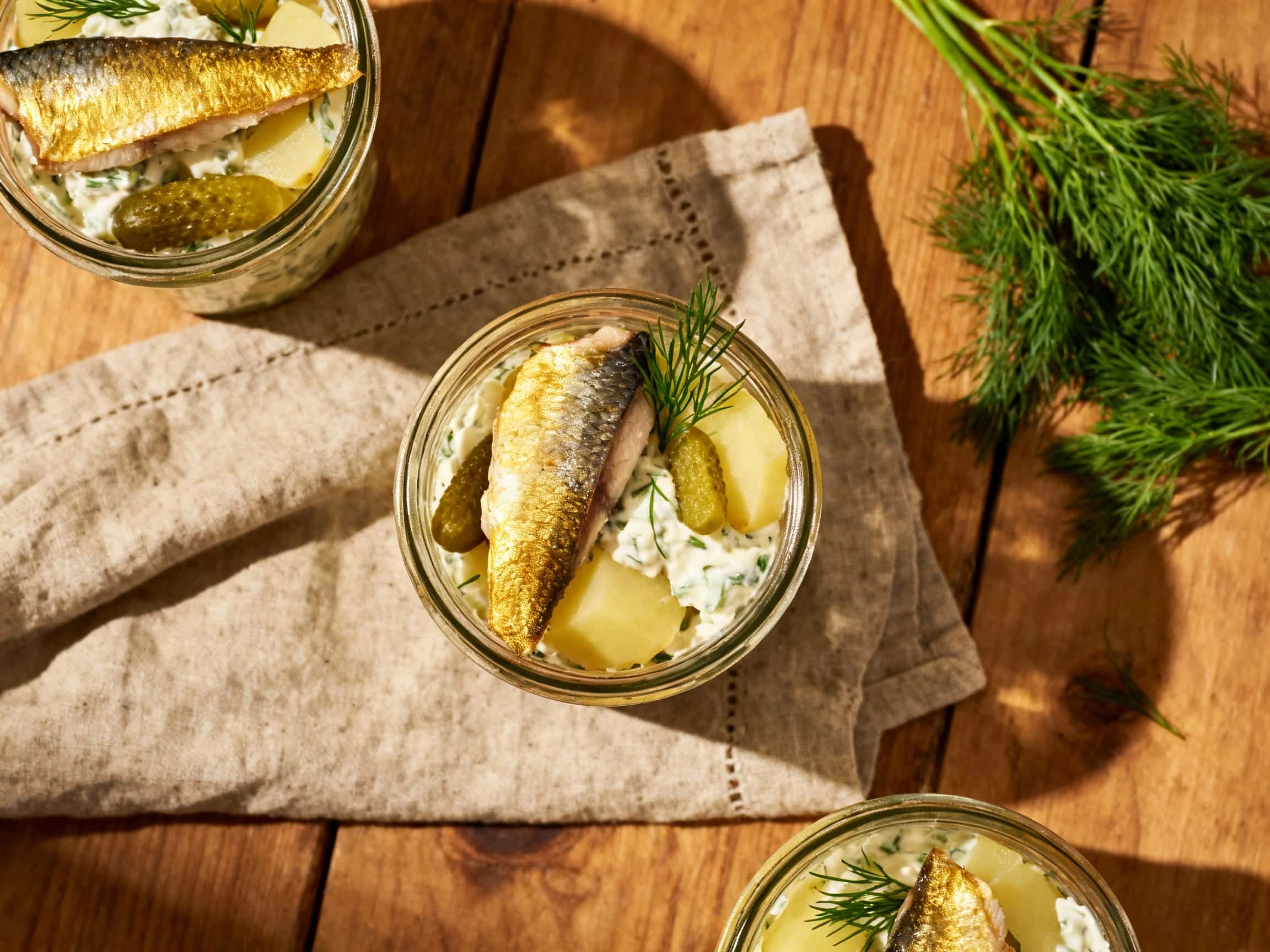 Creamy herring and potato salad is layered in glass jars, topped with fresh dill and red onion, creating a visually appealing and light appetizer.
