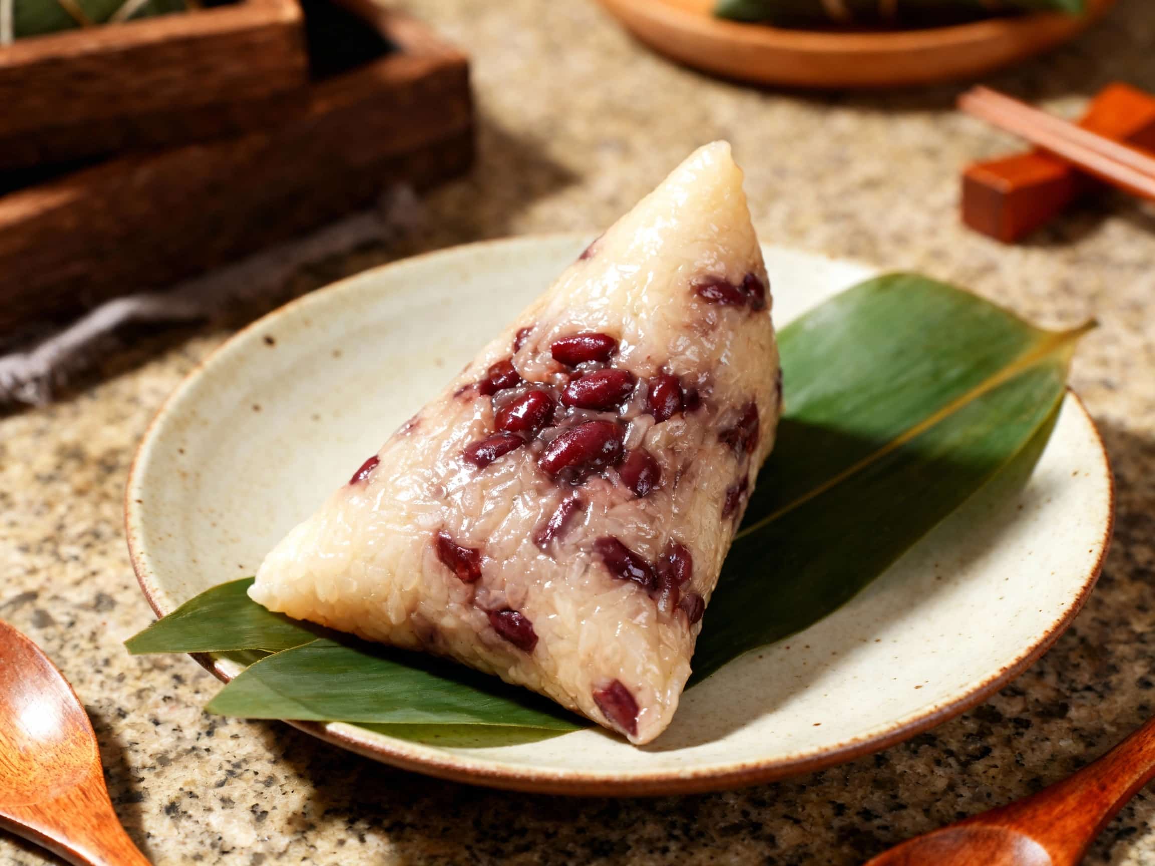 Steamed sticky rice dumplings, known as Zhongzi, are tied with strings, glistening under soft light, promising a sweet red bean paste filling.