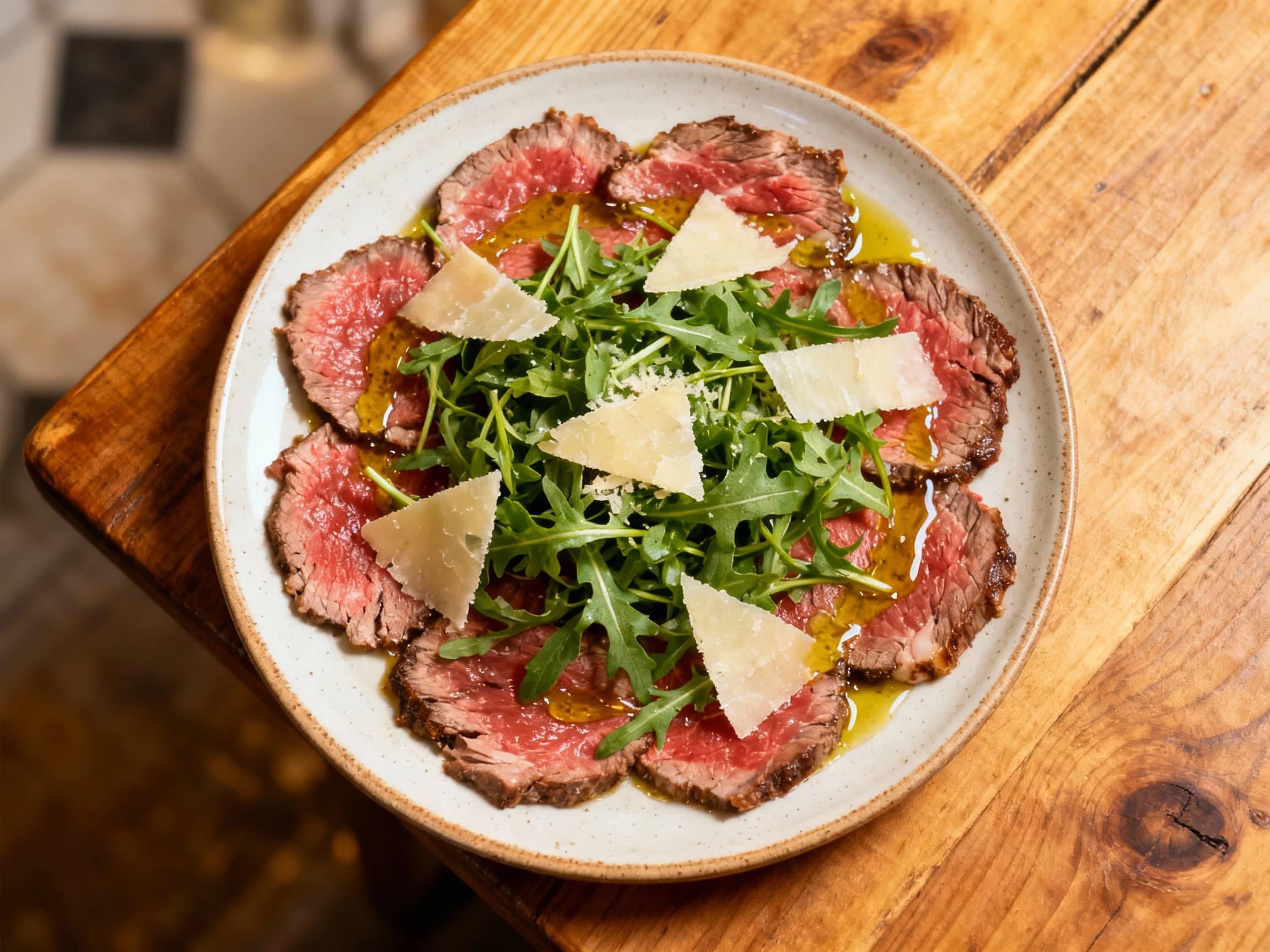 Thinly sliced, ruby-red beef carpaccio is artfully arranged on a bed of peppery arugula, drizzled with olive oil and lemon, and finished with shaved Parmesan cheese.