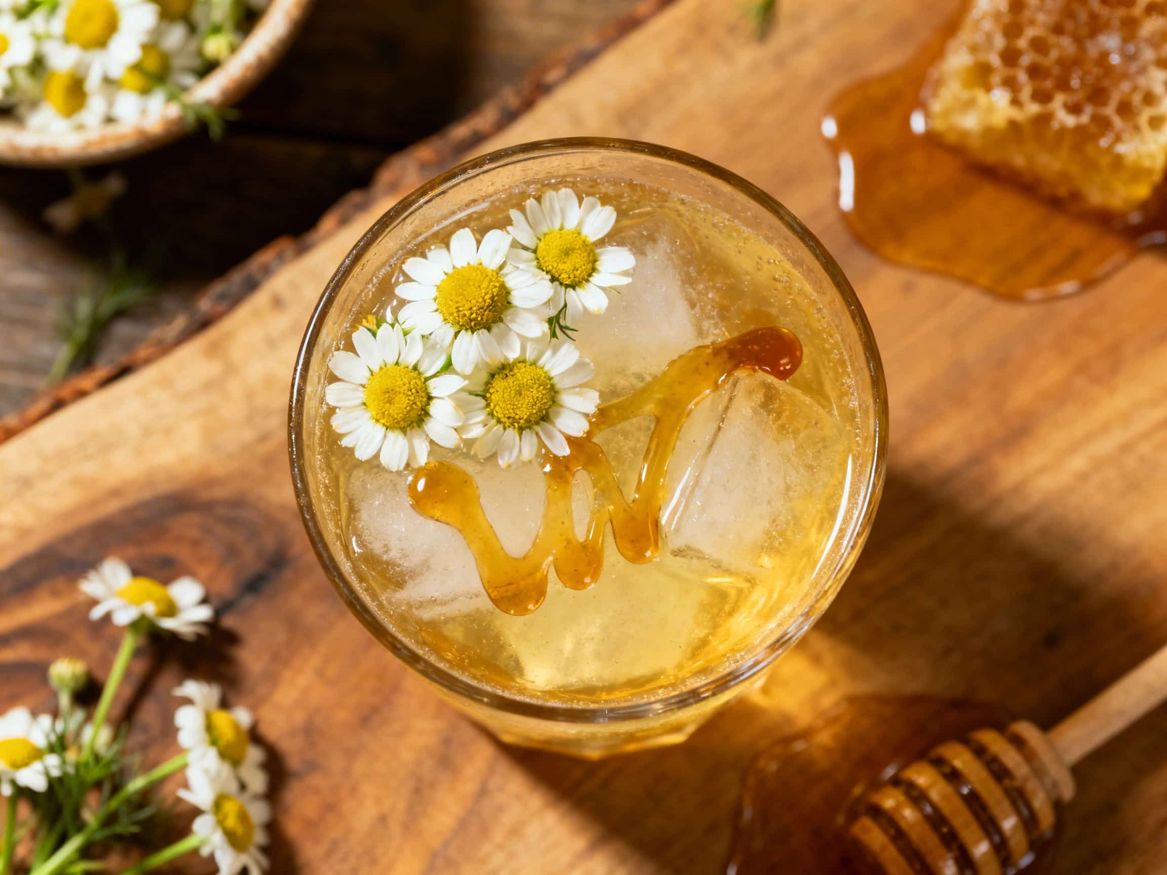A close-up of a refreshing Chamomile Whiskey Smash, a golden-hued tea cocktail served in a chilled rocks glass overflowing with crushed ice. It is elegantly garnished with a bright green mint sprig and a thin lemon wheel on the rim, evoking a sophisticated and comforting atmosphere suitable for relaxation.