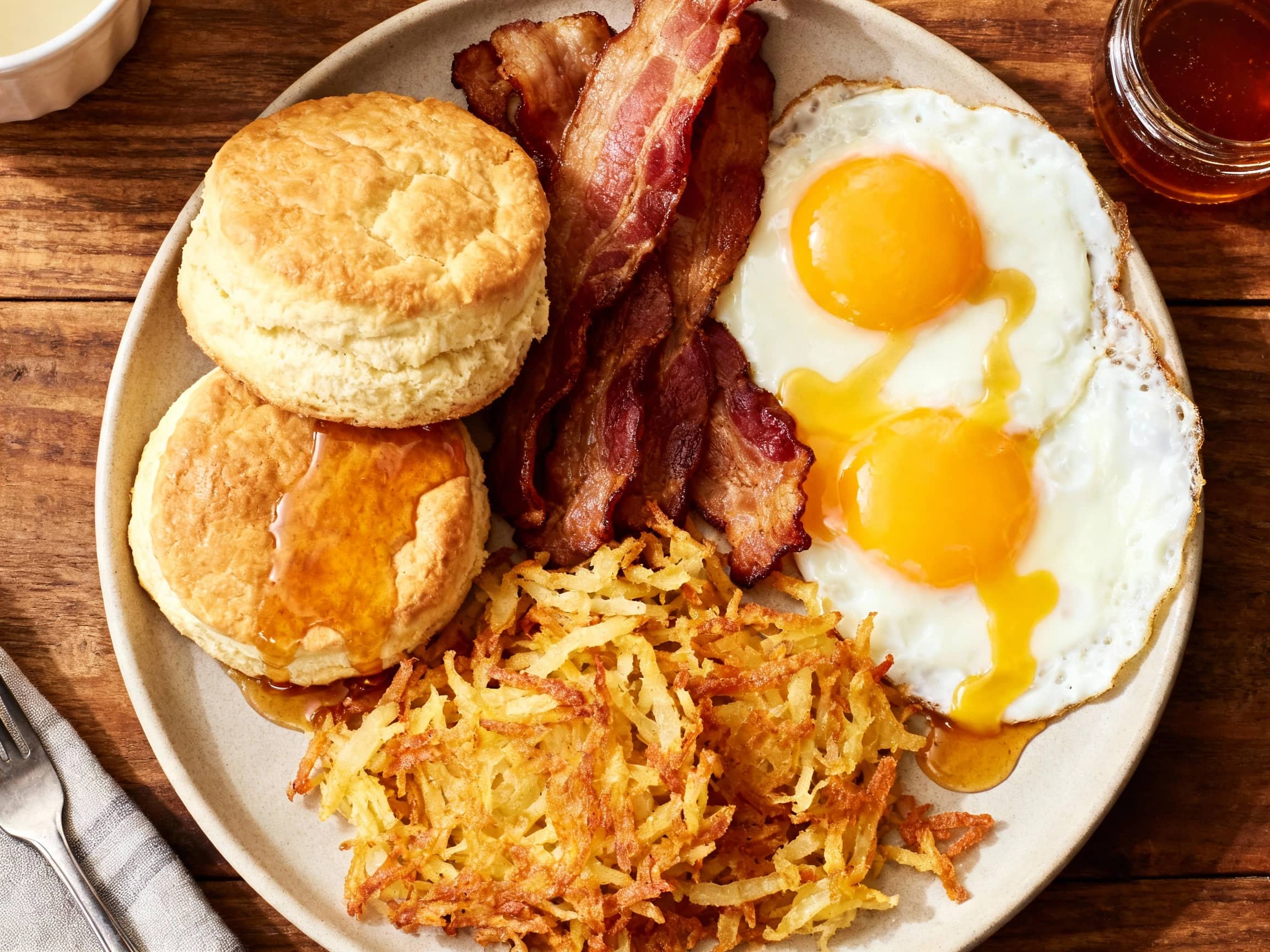 A hearty breakfast platter features perfectly fried eggs, sizzling bacon, and golden-brown hash browns, artfully arranged and ready to fuel your day.