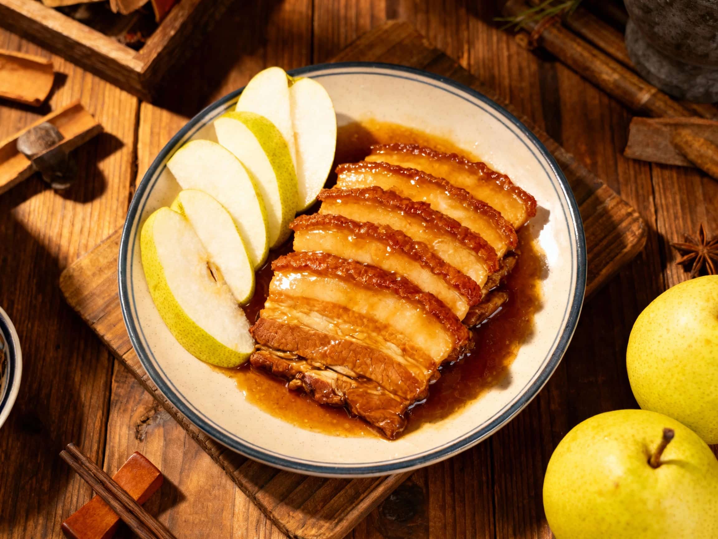 Tender slices of twice-cooked pork, glistening with a sweet and savory Asian pear glaze, are beautifully arranged on a rustic plate, garnished with vibrant green scallions.
