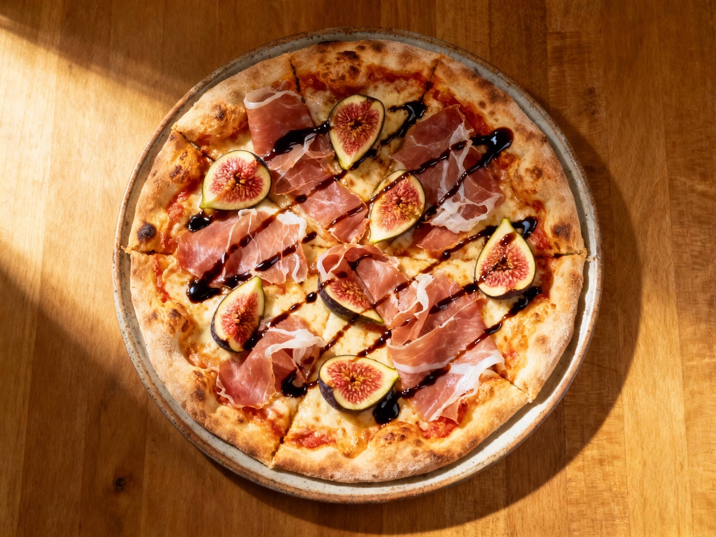 A rustic, thin-crust pizza is topped generously with salty prosciutto, sweet figs, and a drizzle of balsamic glaze, ready to be sliced and enjoyed.