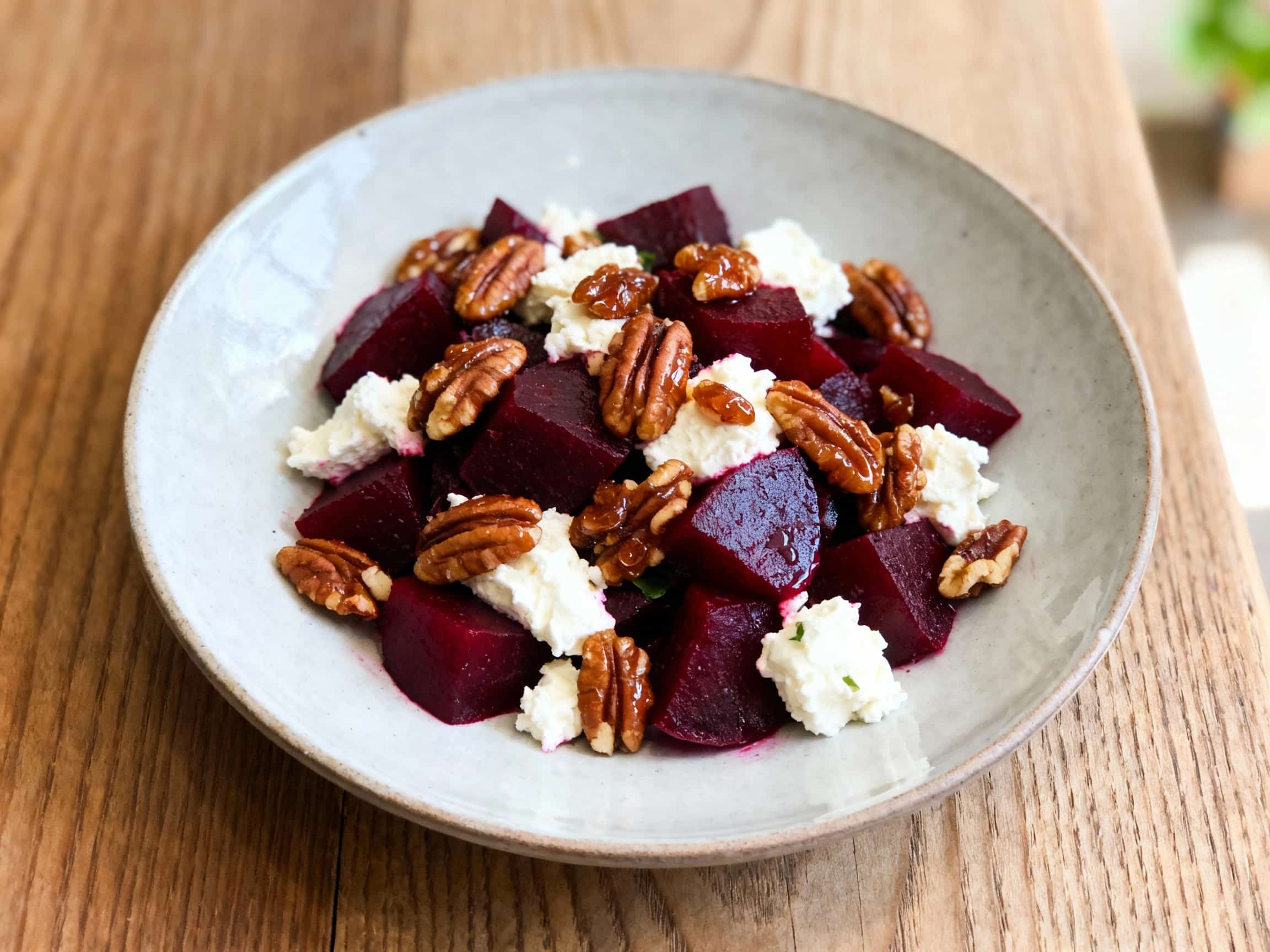 A close-up of a vibrant Roasted Beet and Goat Cheese Salad, presented on a white plate. Earthy red and golden roasted beets are artfully arranged on a bed of fresh arugula, each piece glistening with a light vinaigrette. Creamy white goat cheese crumbles are sprinkled generously over the top, complementing the deep colors. A scattering of shiny, golden-brown candied pecans adds a crunchy texture.