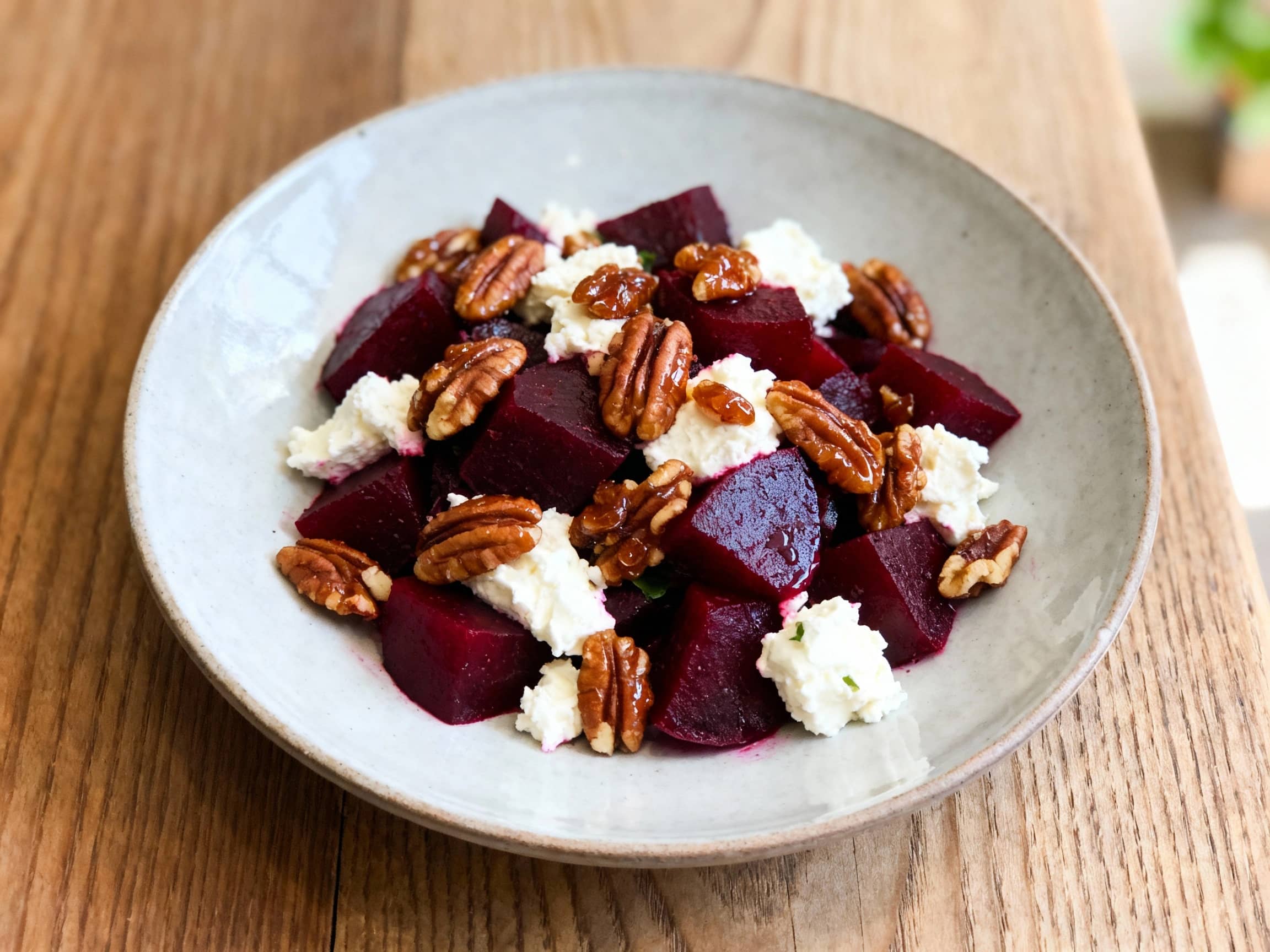 A close-up of a vibrant Roasted Beet and Goat Cheese Salad, presented on a white plate. Earthy red and golden roasted beets are artfully arranged on a bed of fresh arugula, each piece glistening with a light vinaigrette. Creamy white goat cheese crumbles are sprinkled generously over the top, complementing the deep colors. A scattering of shiny, golden-brown candied pecans adds a crunchy texture.