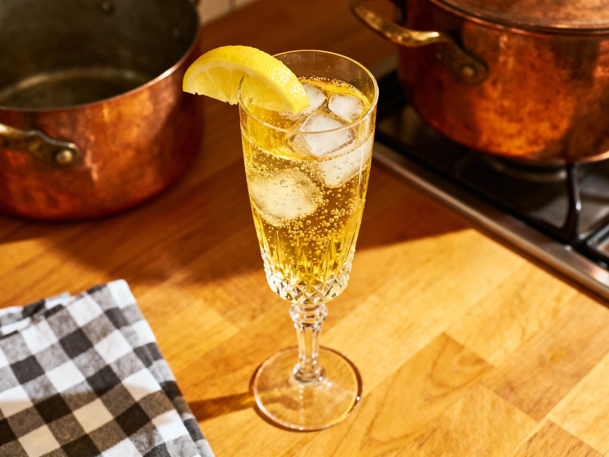 An elegant French 75 cocktail in a tall champagne flute, adorned with a delicate lemon twist. The golden cocktail is visibly bubbly, suggesting its refreshing effervescence, set against a softly blurred, sophisticated background. The glass shows subtle condensation, hinting at its perfectly chilled temperature, making it appear inviting and luxurious.
