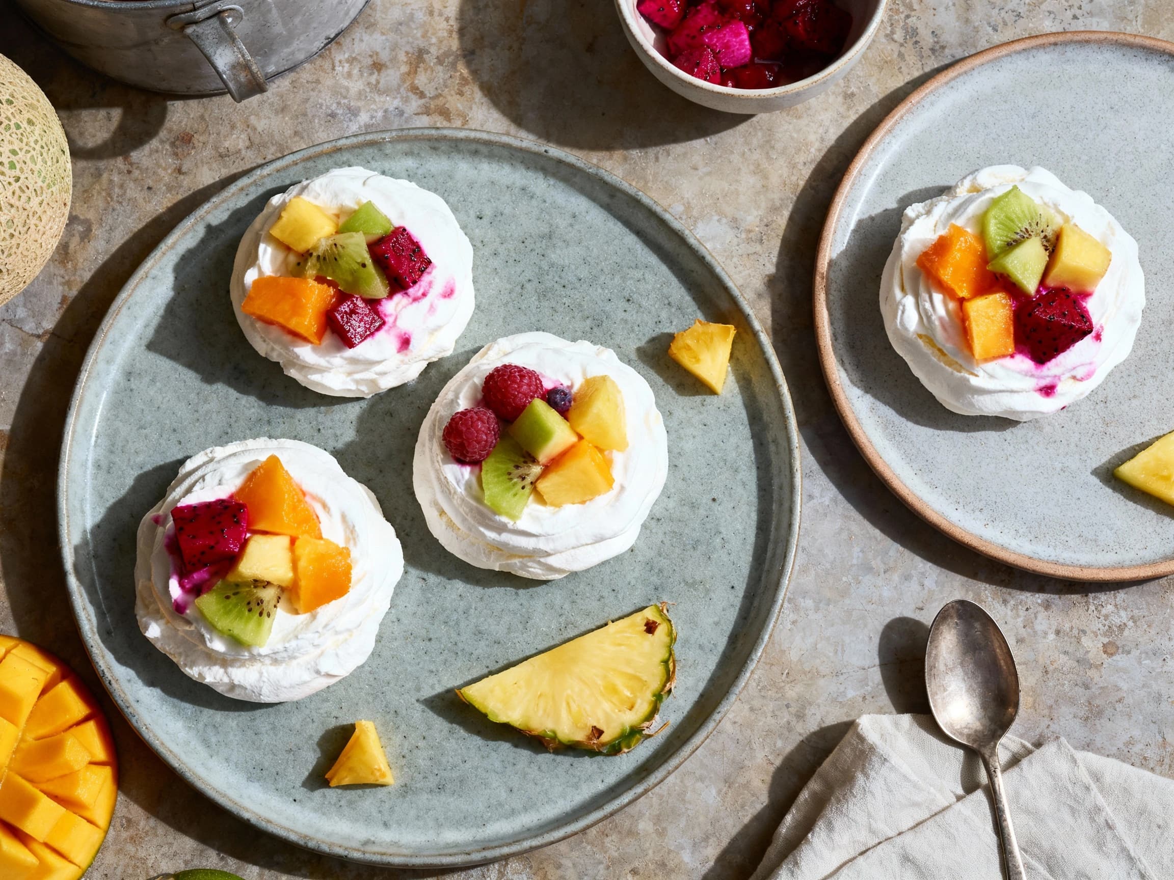 Delicate mini pavlovas topped with luscious whipped cream and a vibrant medley of fresh tropical fruits create a stunning dessert presentation.
